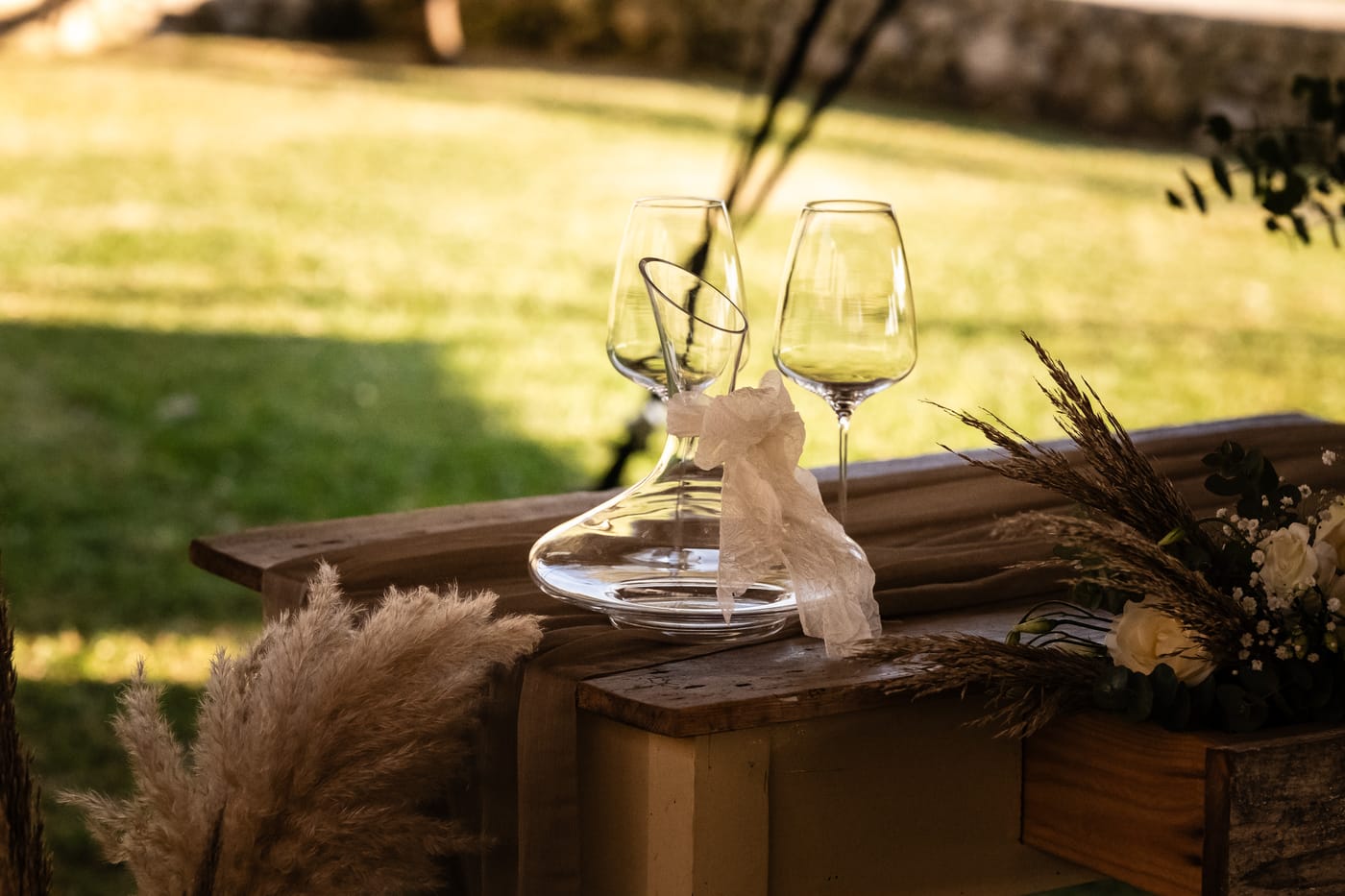 Calici e caraffa su legno nella luce calda del pomeriggio, evento firmato Oniria